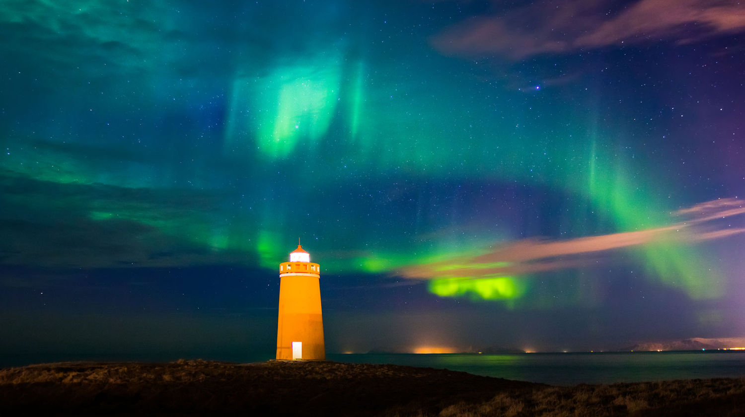 Farol iluminado na Península de Reykjanes, Islândia, sob um céu vibrante com luzes verdes e roxas da aurora boreal