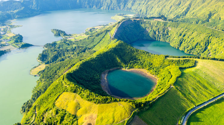 Aerial view of the Sete Cidades volcanic lakes in São Miguel Island, with green fields, crater slopes, and winding roads.