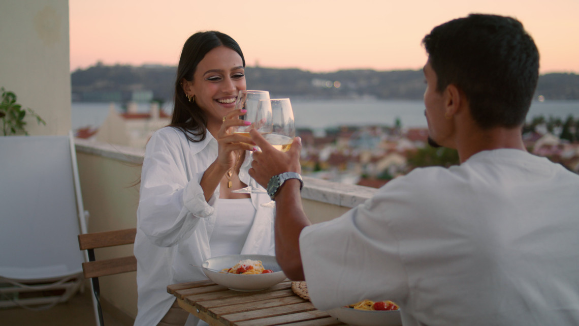 Couple enjoying a romantic dinner with wine on a terrace overlooking Lisbon’s rooftops and the Tagus River at sunset, capturing the charm of all inclusive and cultural getaways in Portugal.