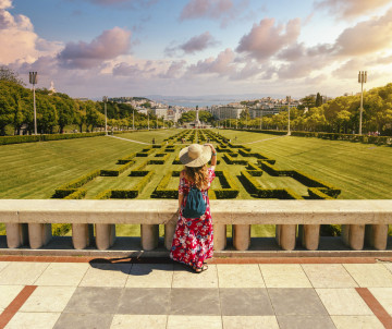A young female tourist in a red floral dress in The Eduardo VII Park under the sunlight in Portugal A young female tourist in a red floral dress in The Eduardo VII Park under the sunlight in Portugal