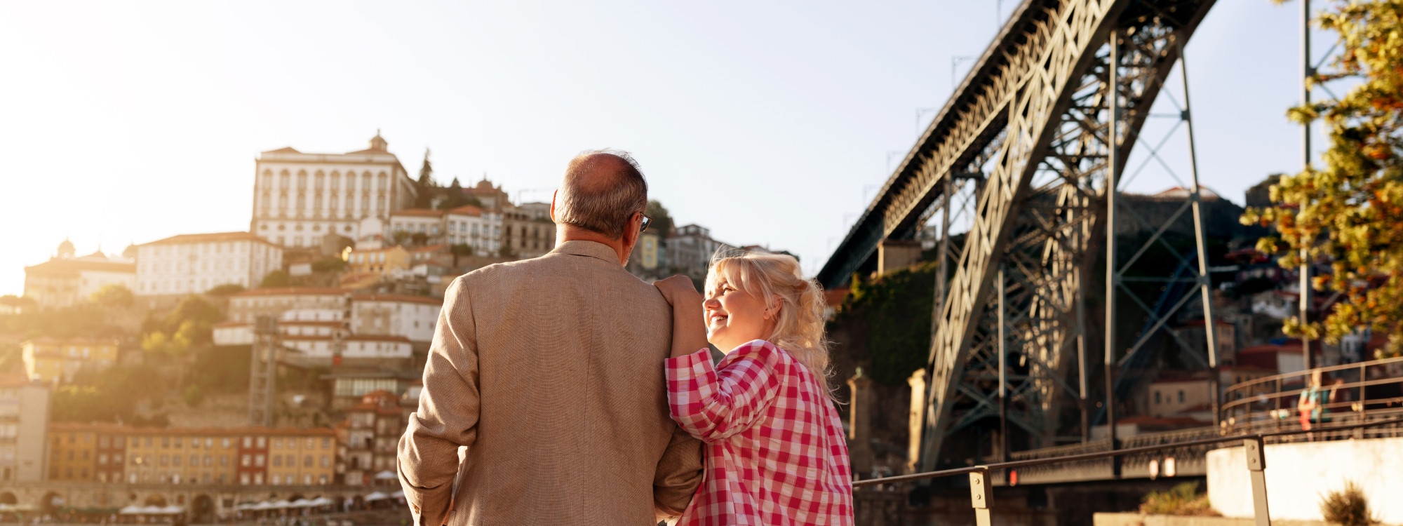 Smiling couple enjoying a scenic moment by the Douro River with a view of the Dom Luís I Bridge and Porto's historic center at sunset