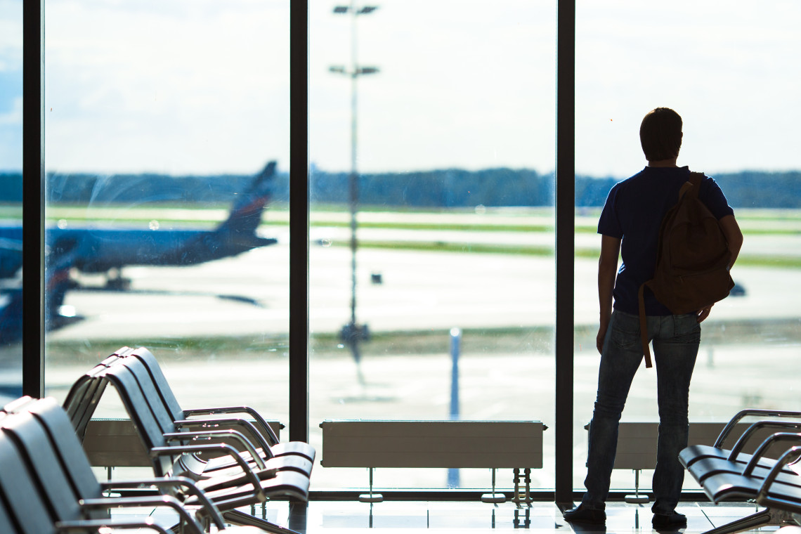 Silhouette of a man with a backpack looking out at airplanes on the runway from inside an airport departure lounge