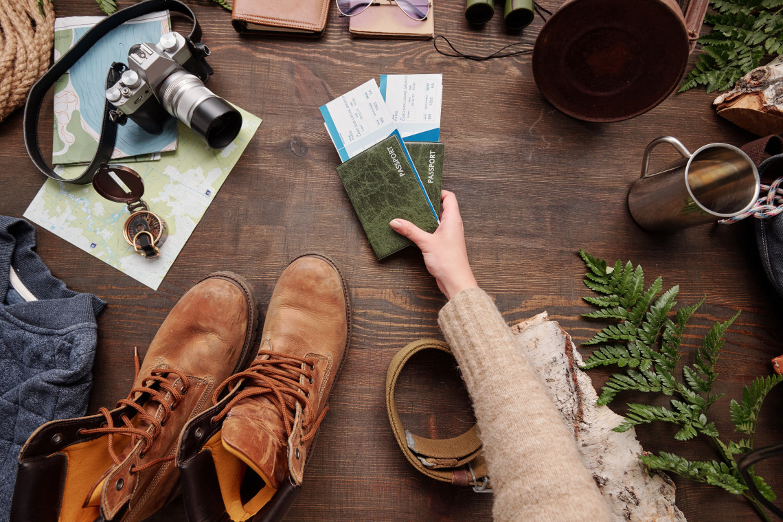 Flat lay of travel essentials including passport, boarding passes, hiking boots, camera, and map on a wooden table