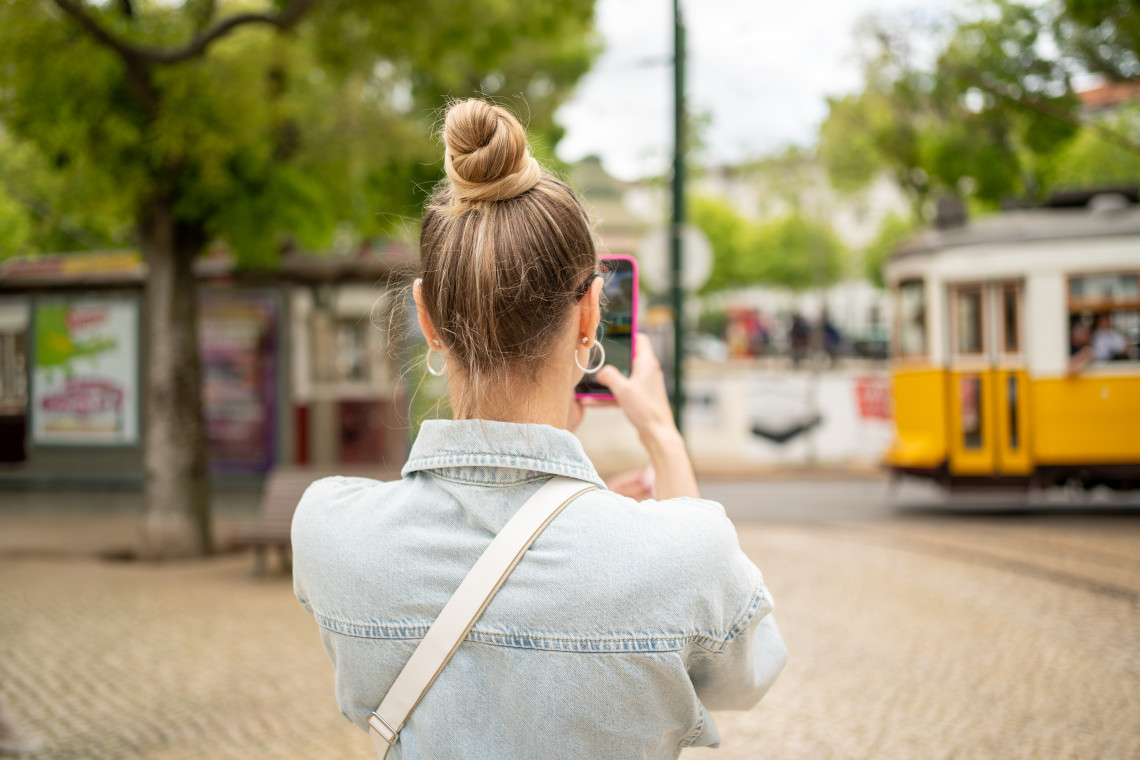 Woman taking a photo of a traditional yellow tram in Lisbon, Portugal, while exploring the city streets