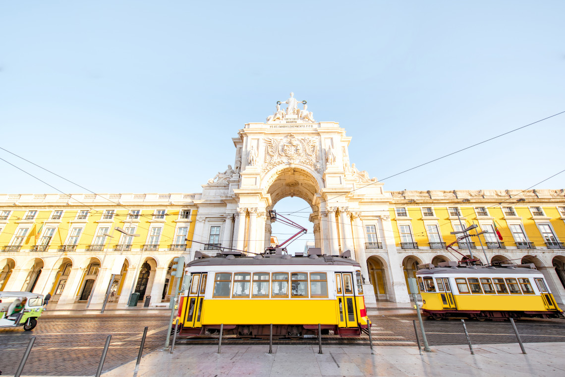Traditional yellow trams passing in front of the grand Arco da Rua Augusta at Praça do Comércio, a historic square in Lisbon, Portugal.