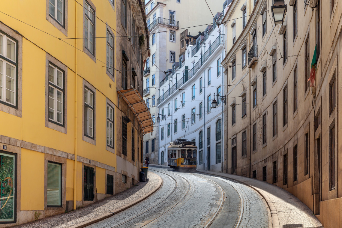 Iconic yellow tram navigating a steep, curved street lined with colorful historic buildings in Lisbon’s old town.