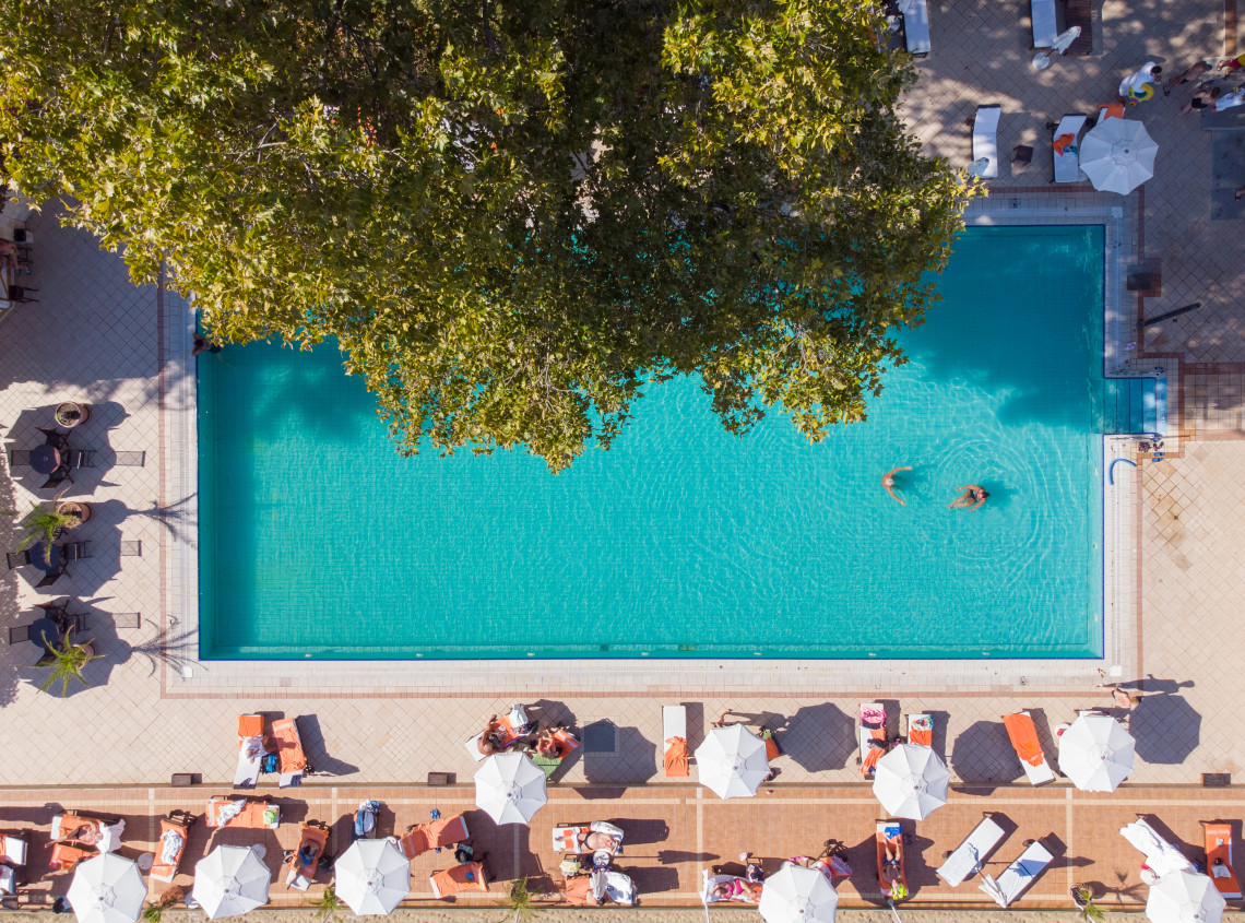 Aerial view of a relaxing hotel swimming pool surrounded by sun loungers and umbrellas in the Algarve, Portugal, with guests enjoying the sunny atmosphere.
