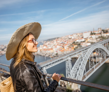 Enjoying the Views Over Porto and the Dom Luís I Bridge Smiling woman in a wide-brimmed hat admiring the panoramic view of Porto, Portugal, with the iconic Dom Luís I Bridge in the background.