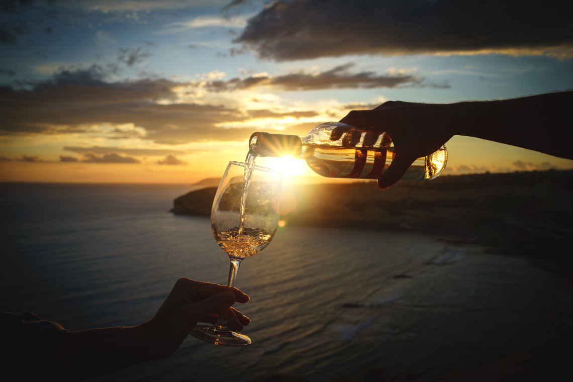 Sunset Wine Experience Over the Ocean – Madeira Island, Portugal Madeira wine being poured into a glass at sunset overlooking the Atlantic Ocean in Madeira Island, Portugal