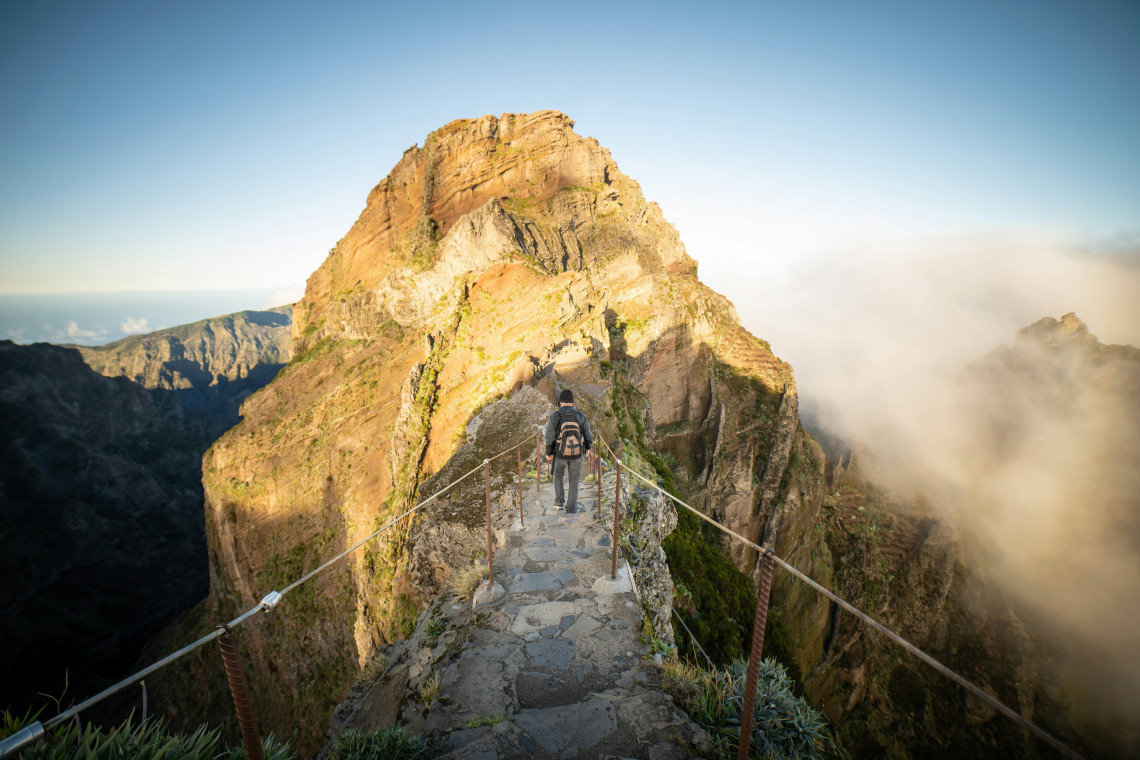 Pico do Arieiro to Pico Ruivo Hike – Mountain Trail in Madeira Island Hiker on the trail between Pico do Arieiro and Pico Ruivo in Madeira Island, Portugal, walking along a dramatic mountain ridge at sunrise