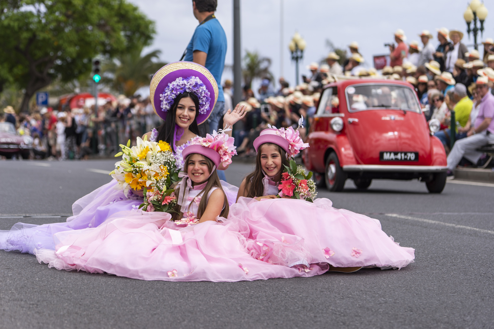 Performers wearing pink and purple floral costumes take part in the Madeira Flower Festival parade in Funchal, Portugal. Spectators line the city street as decorated vehicles and participants move through the annual celebrat