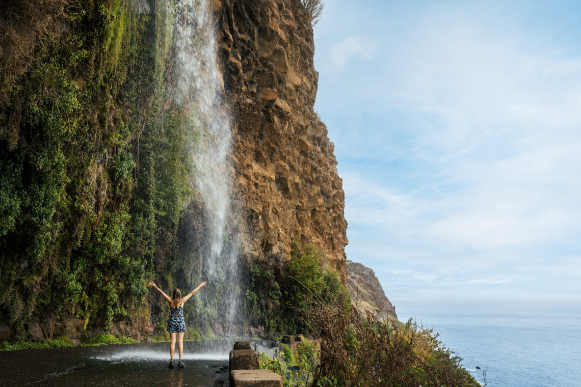 Woman standing under the Angels Waterfall in Madeira Island, Portugal