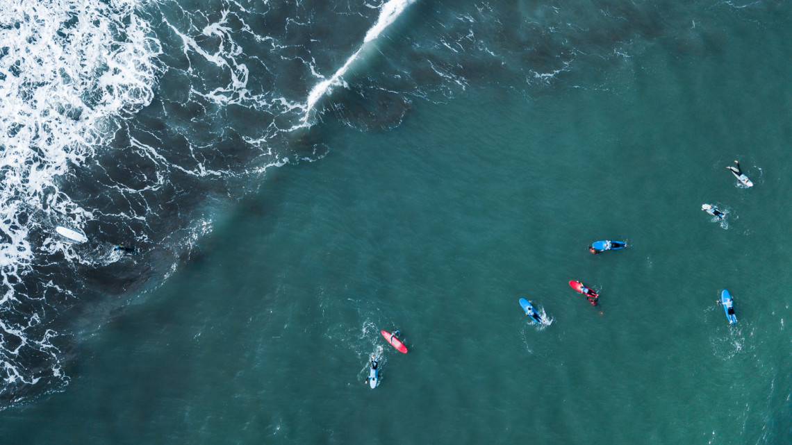 Aerial view of surfer swimming on board near huge blue ocean wave in Porto da Cruz, Madeira island, Portugal