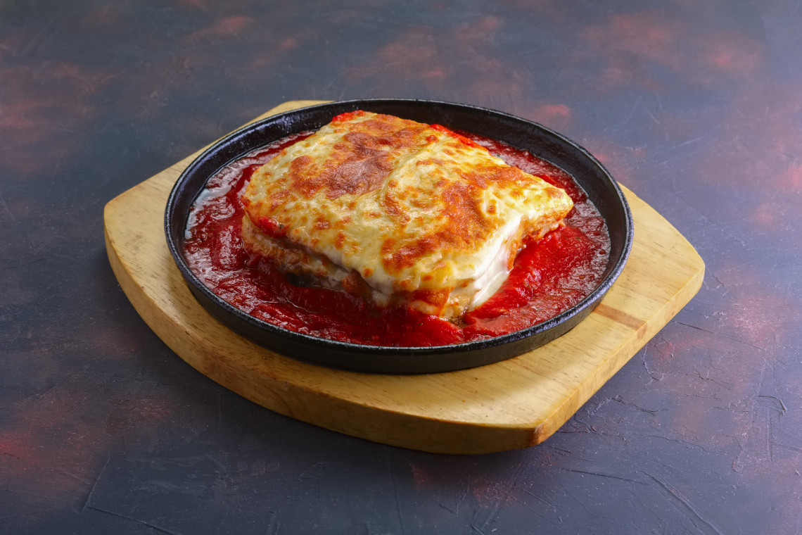 Close-up of a freshly baked Francesinha, a traditional Portuguese sandwich covered in melted cheese and spicy tomato sauce, served in a hot skillet.