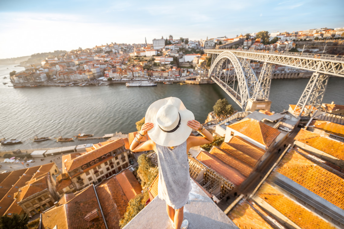 Woman enjoying the scenic view of Porto from Vila Nova de Gaia, overlooking the Douro River and the iconic Dom Luís I Bridge at sunset.