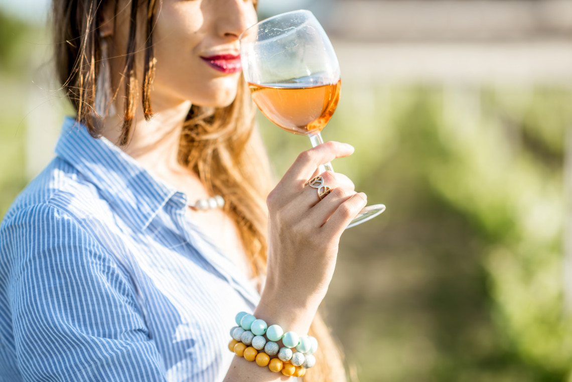 Close-up of a woman tasting rosé wine in a vineyard in Portugal, wearing colorful bracelets and a striped shirt, capturing the essence of a wine-tasting experience.