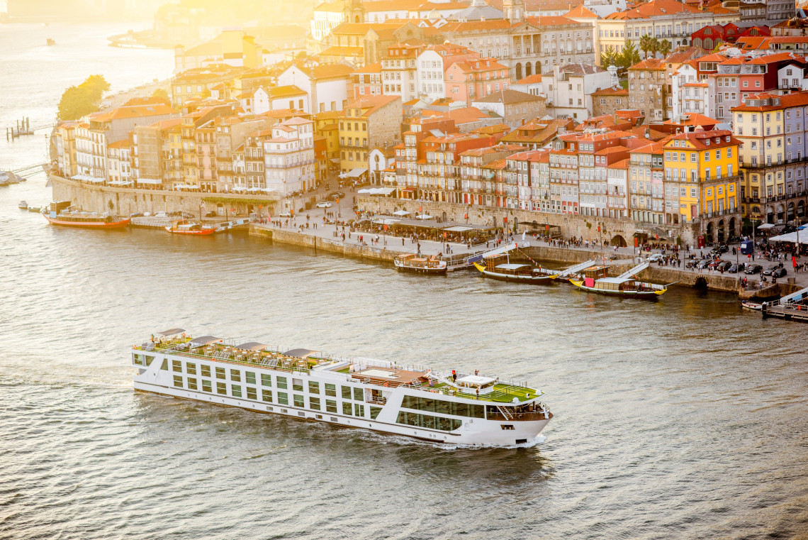 Luxury river cruise boat sailing on the Douro River with Porto’s historic Ribeira district and colorful waterfront buildings in the background.