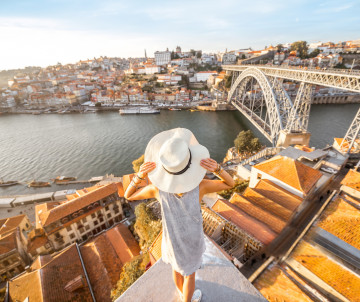 Woman in a white hat admiring the view of Porto and the Dom Luís I Bridge from above at sunset.