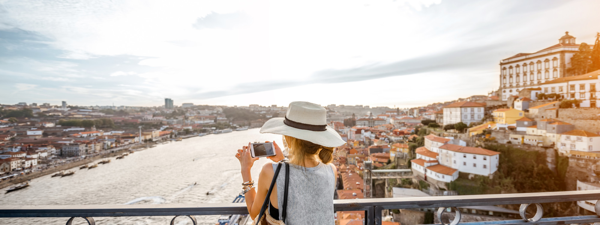 Traveler taking photos of Porto’s Douro River and colorful riverside rooftops, included in Black Friday vacation packages.