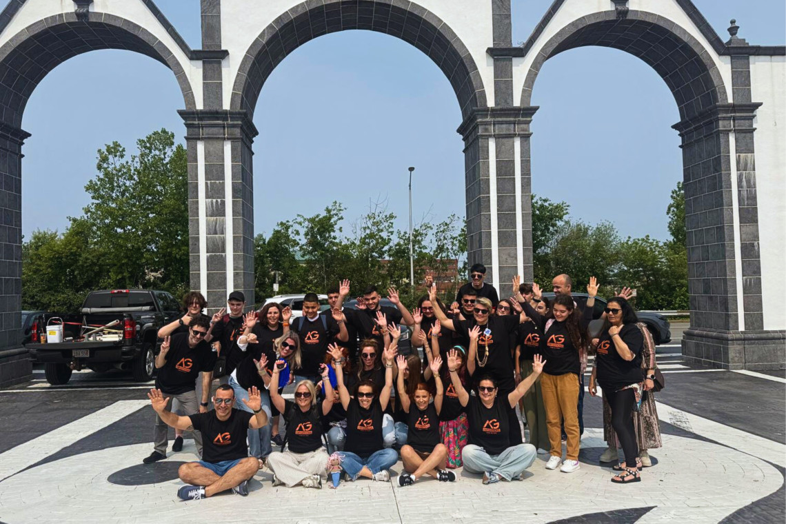 A group of local kids and teens participating in AG Expeditions’ community program, smiling and waving in front of the iconic Portas da Cidade arches in Ponta Delgada, São Miguel Island, Azores