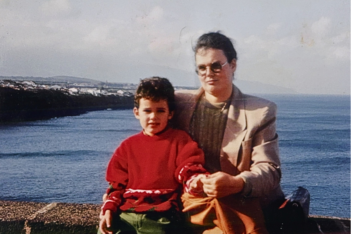 A childhood photo of Luís Nunes sitting beside his mother on a viewpoint above the ocean in Rabo de Peixe, São Miguel Island, Azores, with coastal landscapes stretching into the distance