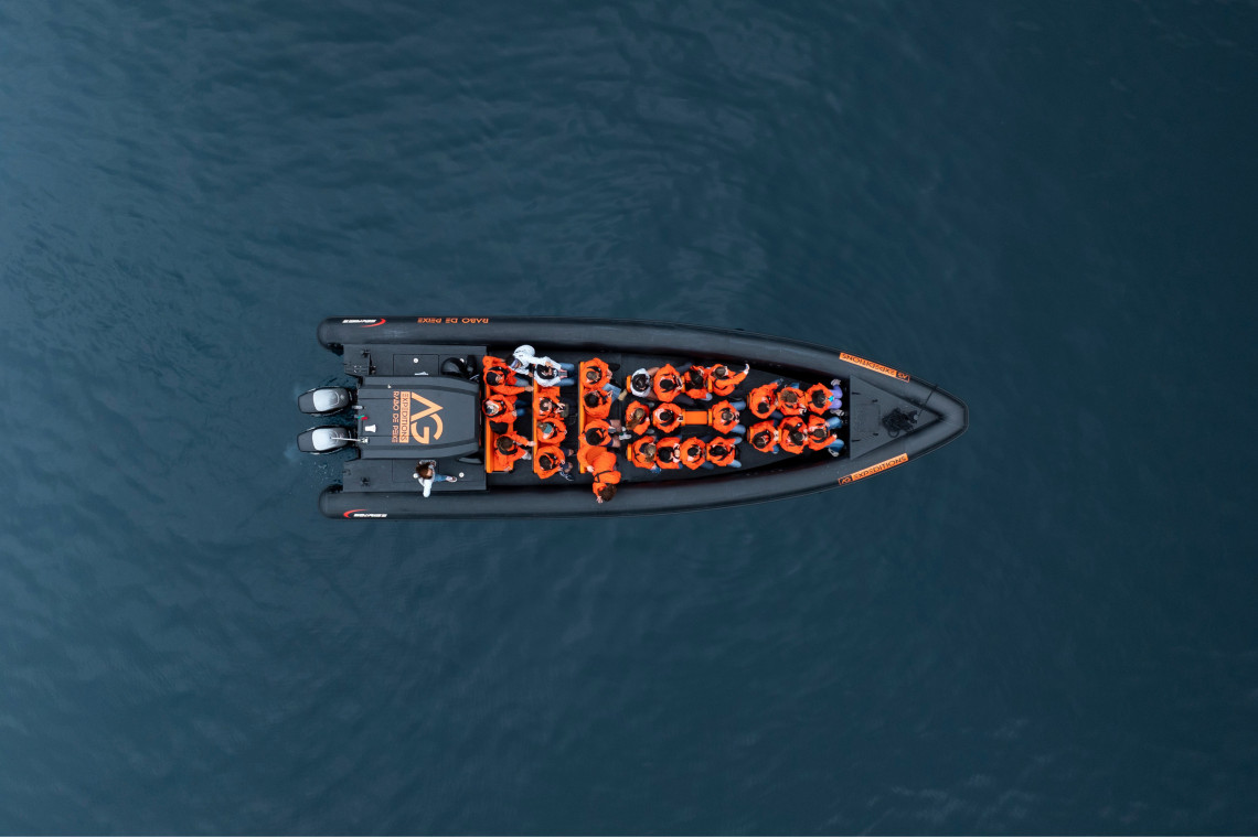 Aerial view of an AG Expeditions speed boat with passengers in orange life vests cruising the ocean off São Miguel Island, Azores.