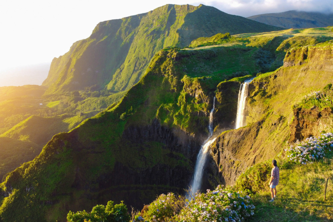 Poço da Ribeira do Ferreiro waterfall on Flores Island, Azores, surrounded by lush green cliffs and wildflowers at sunset
