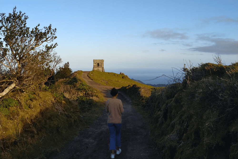 Trail path to Castelo Branco Viewpoint, in Ponta Garça, São Miguel. Woman walking toward the iconic tower at Castelo Branco viewpoint, in Ponta Garça, São Miguel Island, Azores, with ocean views at sunset.