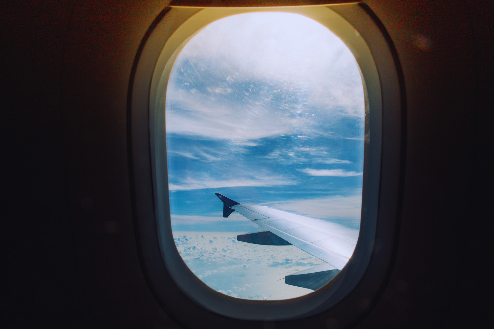 Airplane wing and clouds seen through window during flight
