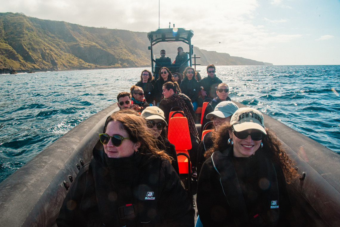 Group of people on a speed boat enjoying a coastal tour near the cliffs of São Miguel Island in the Azores on a sunny day.