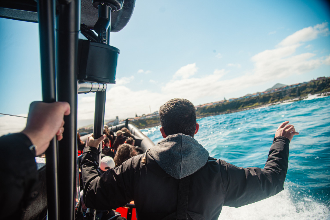 View from an AG Expeditions speed boat tour near the coast of São Miguel Island, Azores, with a guide standing and guests enjoying the ocean ride.