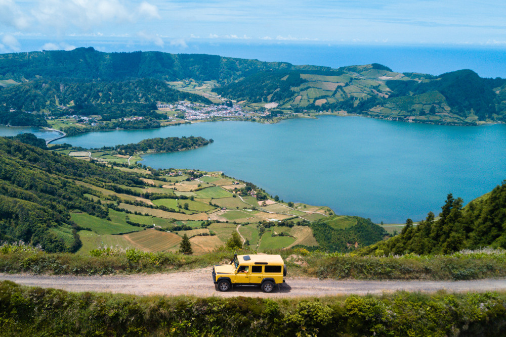 Yellow jeep driving along a dirt trail with panoramic views of Sete Cidades crater lakes in São Miguel, Azores