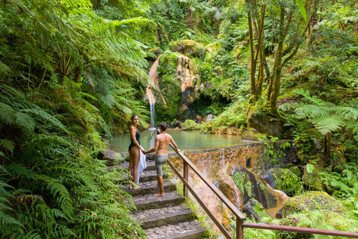 Couple entering the lush thermal pools surrounded by forest at Caldeira Velha in São Miguel, Azores