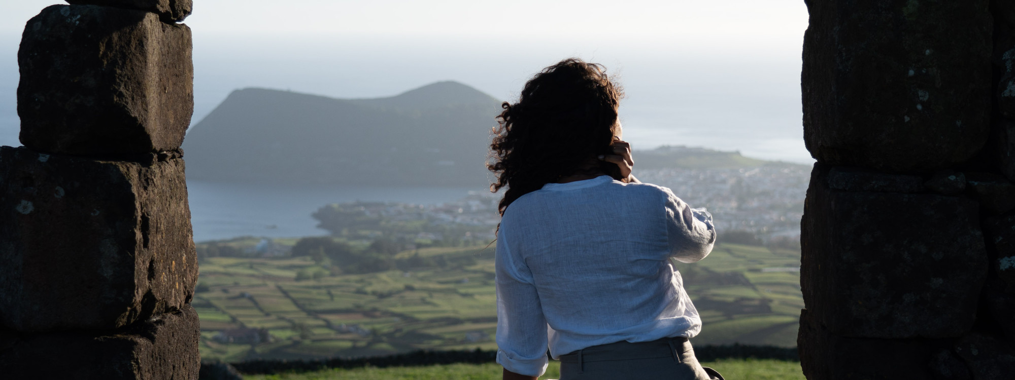 Viewpoint in Ribeirinha overlooking Angra do Heroísmo and Monte Brasil – Terceira Island, Azores Woman admiring the view over Angra do Heroísmo and Monte Brasil from a stone lookout in Ribeirinha, Terceira Island, Azores