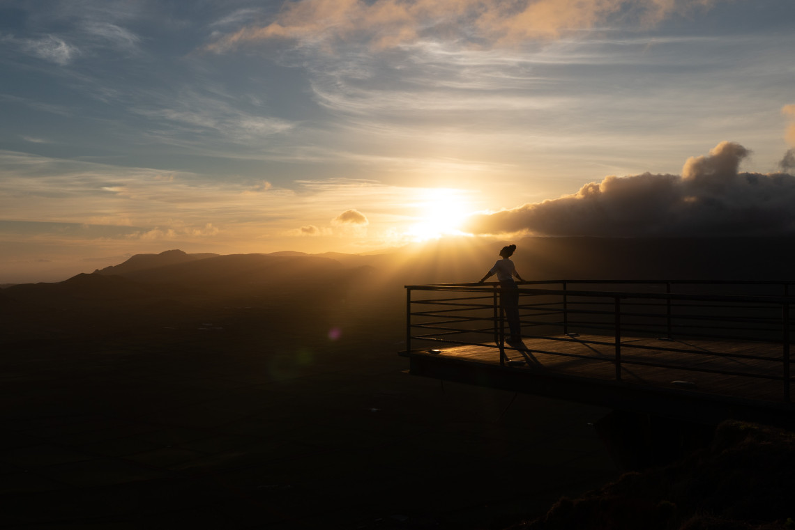 Woman watching the sunset from the Serra do Cume viewpoint on Terceira Island, Azores, with panoramic views over the island’s green patchwork fields
