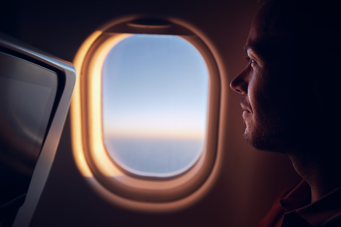 Man looking out airplane window at sunset during flight, enjoying peaceful travel moments in the sky