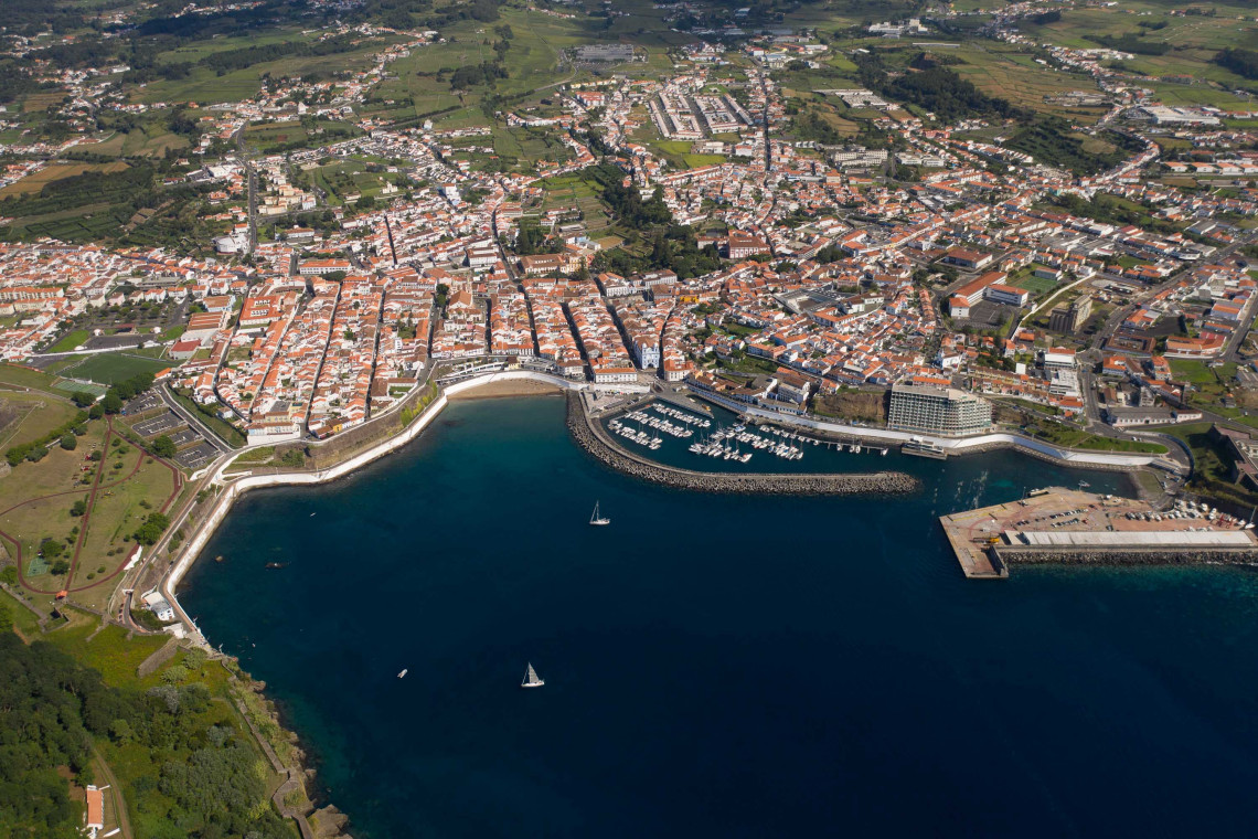 Aerial view of Angra do Heroísmo and its marina on Terceira Island, Azores, with red-roofed houses and green countryside in the background
