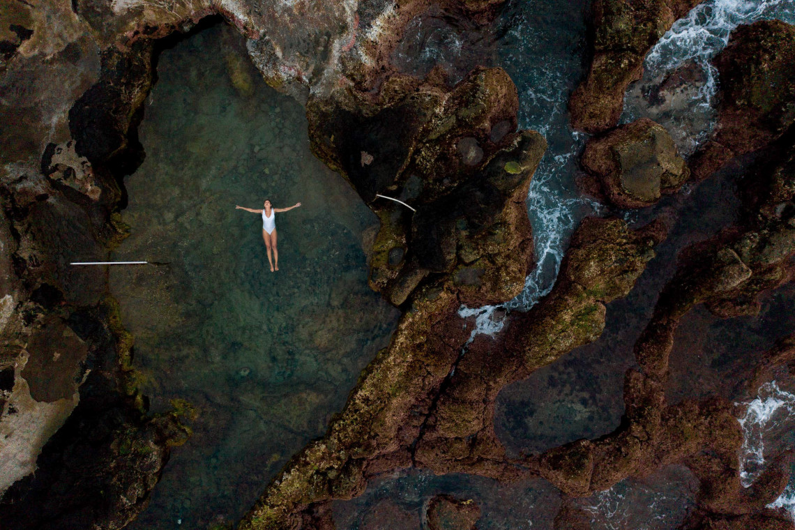 Woman floating in a volcanic rock tidal pool by the ocean on Terceira Island, Azores, enjoying a peaceful moment in nature