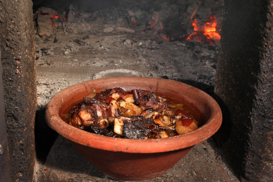 Traditional Azorean alcatra beef stew slow-cooking in a clay pot inside a wood-fired oven on Terceira Island, Azores