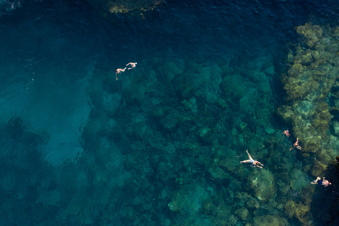 Aerial view of people swimming in crystal-clear turquoise water above volcanic rock formations on Terceira Island, Azores
