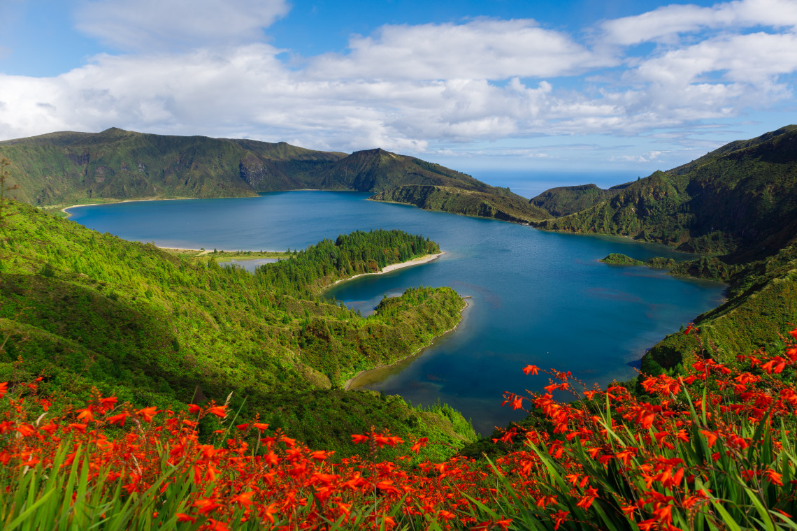 Lagoa do Fogo, São Miguel Island, Azores Panoramic view of Lagoa do Fogo surrounded by lush green mountains and red wildflowers on São Miguel Island, Azores