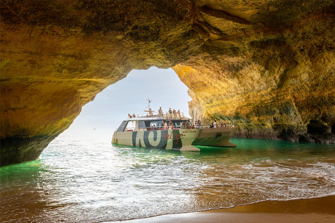 Tour boat entering the Benagil Cave in Algarve, Portugal, with passengers on board viewing the cave’s rocky interior and turquoise waters from the sea