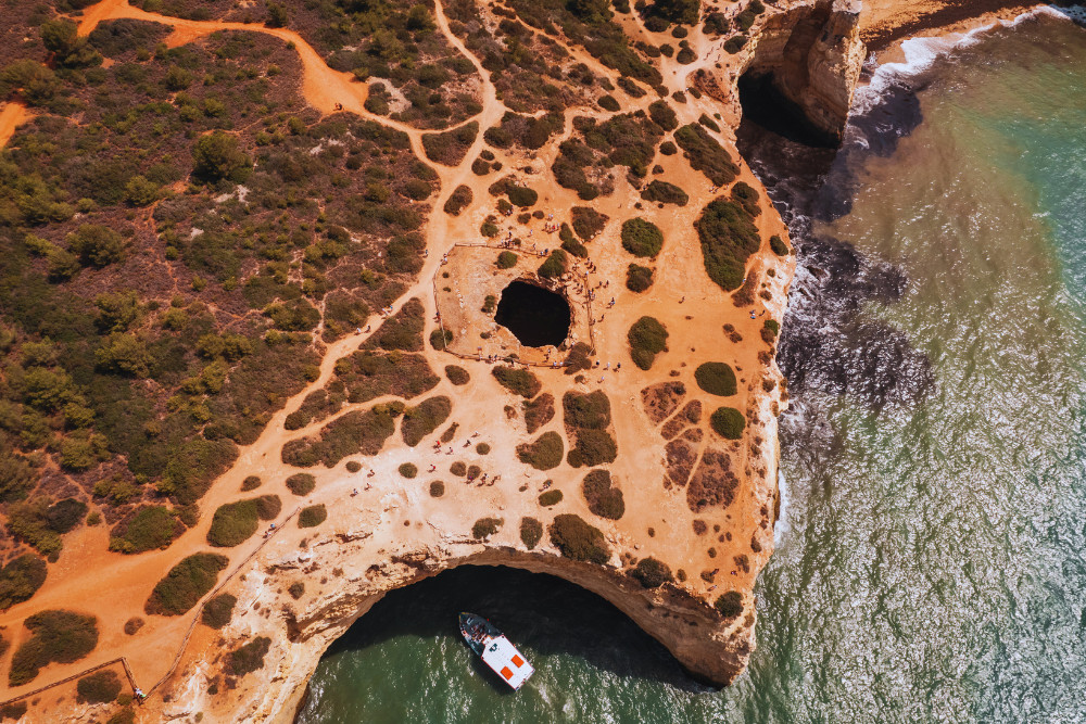 Drone shot of the Benagil Cave in Algarve, Portugal, showing the cave’s iconic skylight, surrounding cliffs, and a boat near the sea cave entrance
