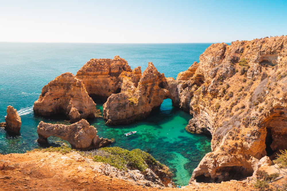 Panoramic view of Ponta da Piedade in Lagos, Algarve, Portugal, showcasing dramatic limestone cliffs, turquoise water, sea arches, and a small boat exploring the natural formations